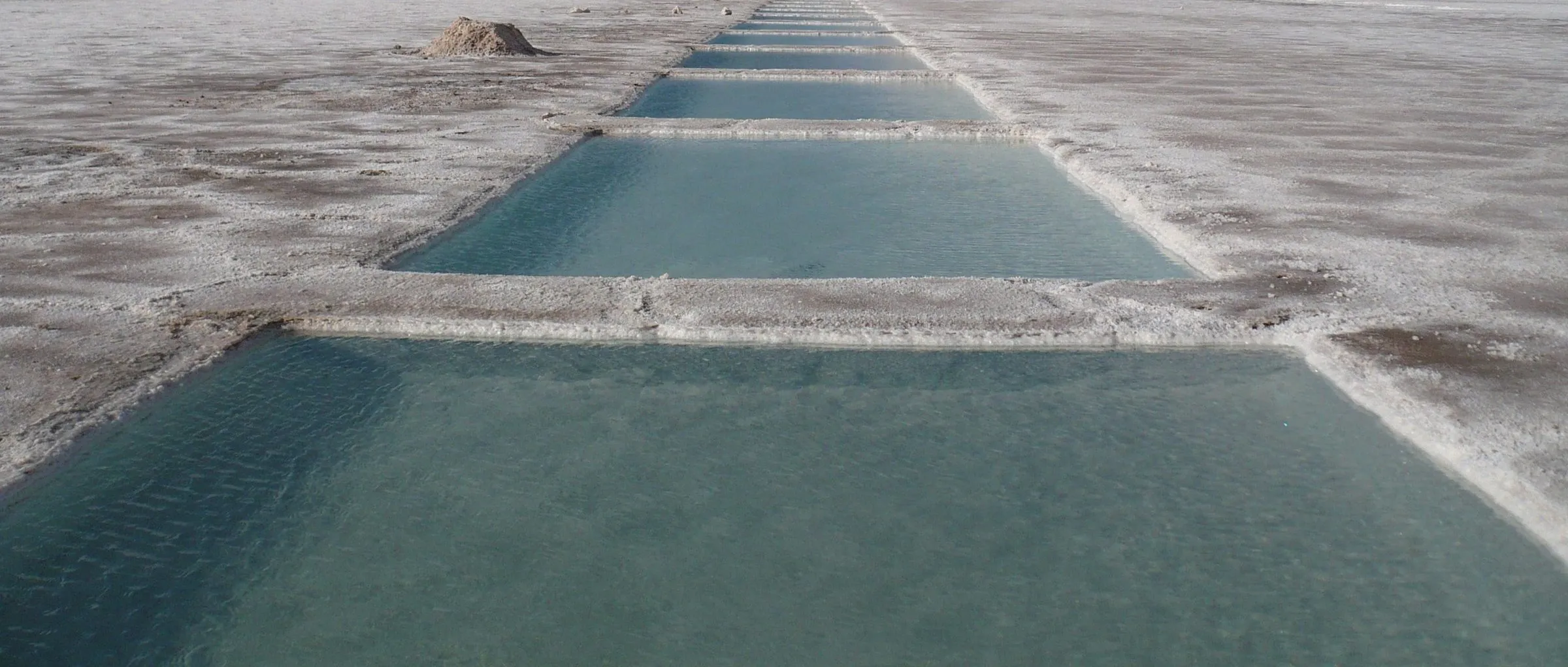 Piletas de agua turquesa sobre la sal blanca de Salinas Grandes, Jujuy, en perspectiva hacia el horizonte.